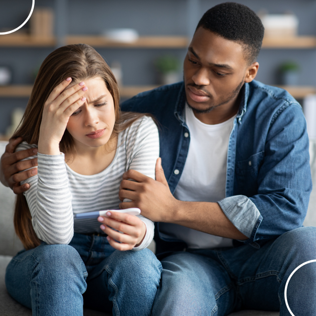 A couple embracing, looking sad, with the woman holding a negative pregnancy test. This image reflects the emotional impact of sperm disorders on fertility.