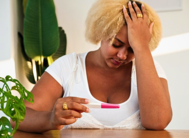 Young African American woman looking upset while holding a negative pregnancy test, reflecting emotions tied to moving ahead after a failed or several failed fertility treatments: finding strength and hope.