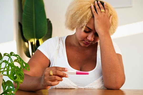 Young African American woman looking upset while holding a negative pregnancy test, reflecting emotions tied to moving ahead after a failed or several failed fertility treatments: finding strength and hope.