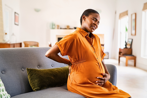 A pregnant woman experiencing backache while sitting on the sofa – Navigating Fear and Anxiety During the IVF Journey.