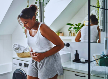 Young African-American woman standing in the bathroom, experiencing stomach pain from holiday health risks.