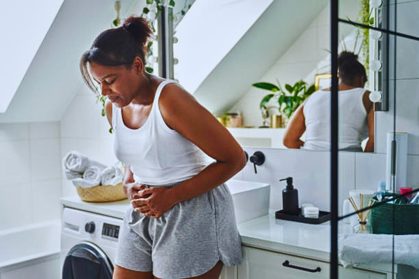 Young African-American woman standing in the bathroom, experiencing stomach pain from holiday health risks.