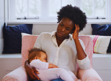 Exhausted new mother experiencing mother sleep deprivation, gently holding her sleeping baby daughter in a nursery at home, showing signs of postnatal depression
