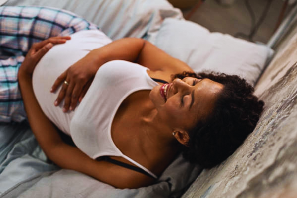 Smiling pregnant woman lying comfortably on her bed while monitoring for signs of third-trimester bleeding to ensure a safe pregnancy