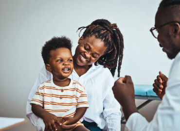Mother and doctor performing a pediatric checkup for a smiling boy, promoting child health and wellness in a supportive medical environment.