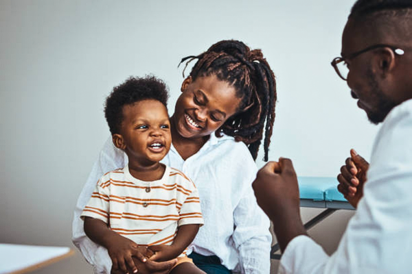 Mother and doctor performing a pediatric checkup for a smiling boy, promoting child health and wellness in a supportive medical environment.