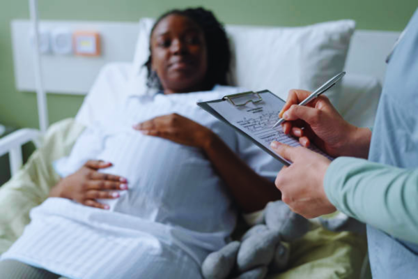 Pregnant woman lying in a hospital bed, consulting with a doctor holding a clipboard and pen, highlighting attentive patient care and hospital room environment, with focus on safe childbirth