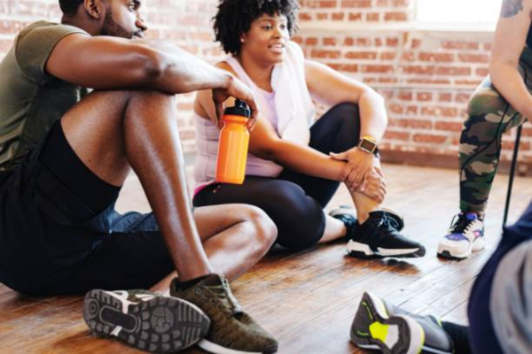 Group of African American men and women in athletic wear taking a break after exercise, symbolizing teamwork and motivation in their fitness journey.